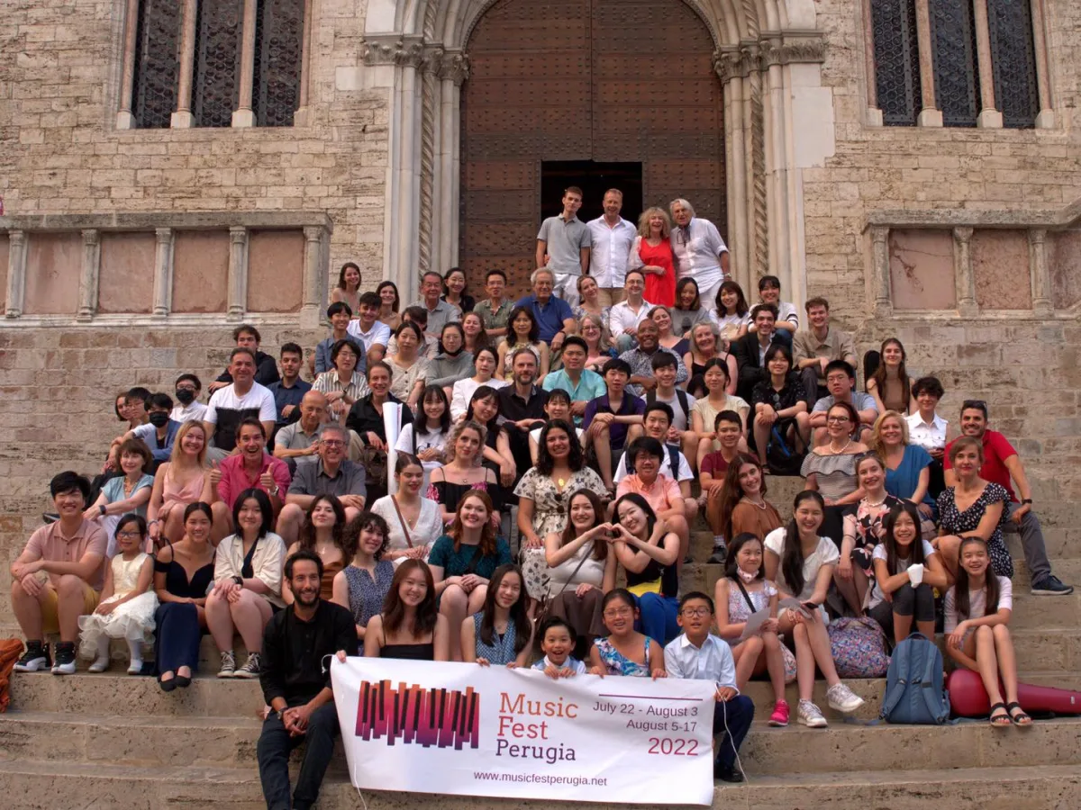 Eine große Festivalgruppe sitzt hinter einem Banner auf Kirchenstufen