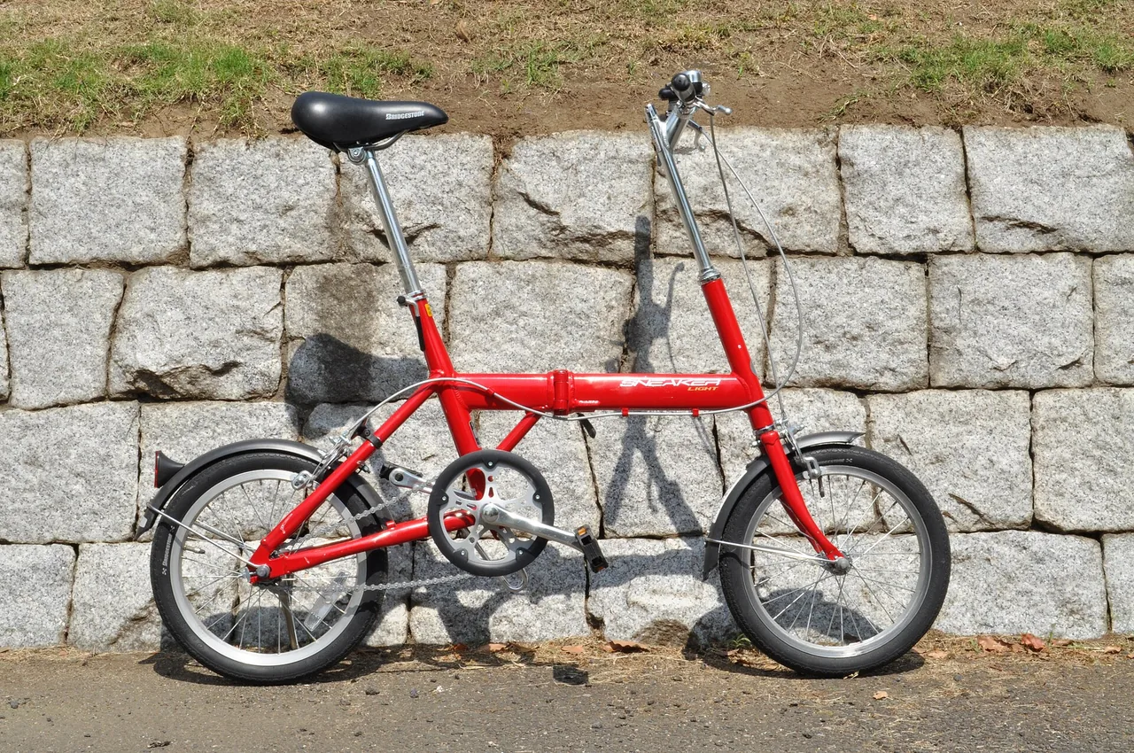 La stessa bici pieghevole rossa appoggiata a un muro di pietra
