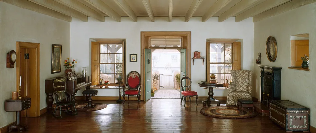 A wide, low photo of a period living room with a piano and wooden floor