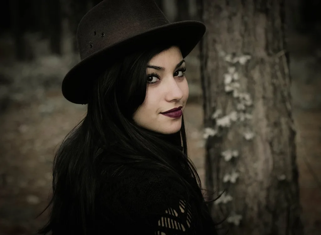 A woman in a black hat looking back over her shoulder in a dark forest, landscape frame