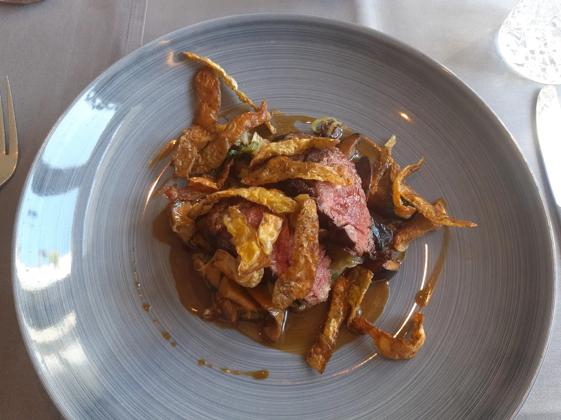 Una bistecca a fette con chips di patate e salsa su un piatto grigio, su una tovaglia chiara con le posate sul bordo