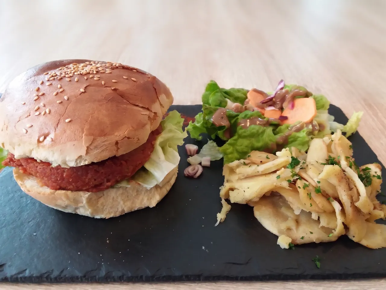 Lo stesso burger sullo stesso tagliere, senza bicchieri né saliera, su un tavolo di legno dai toni morbidi