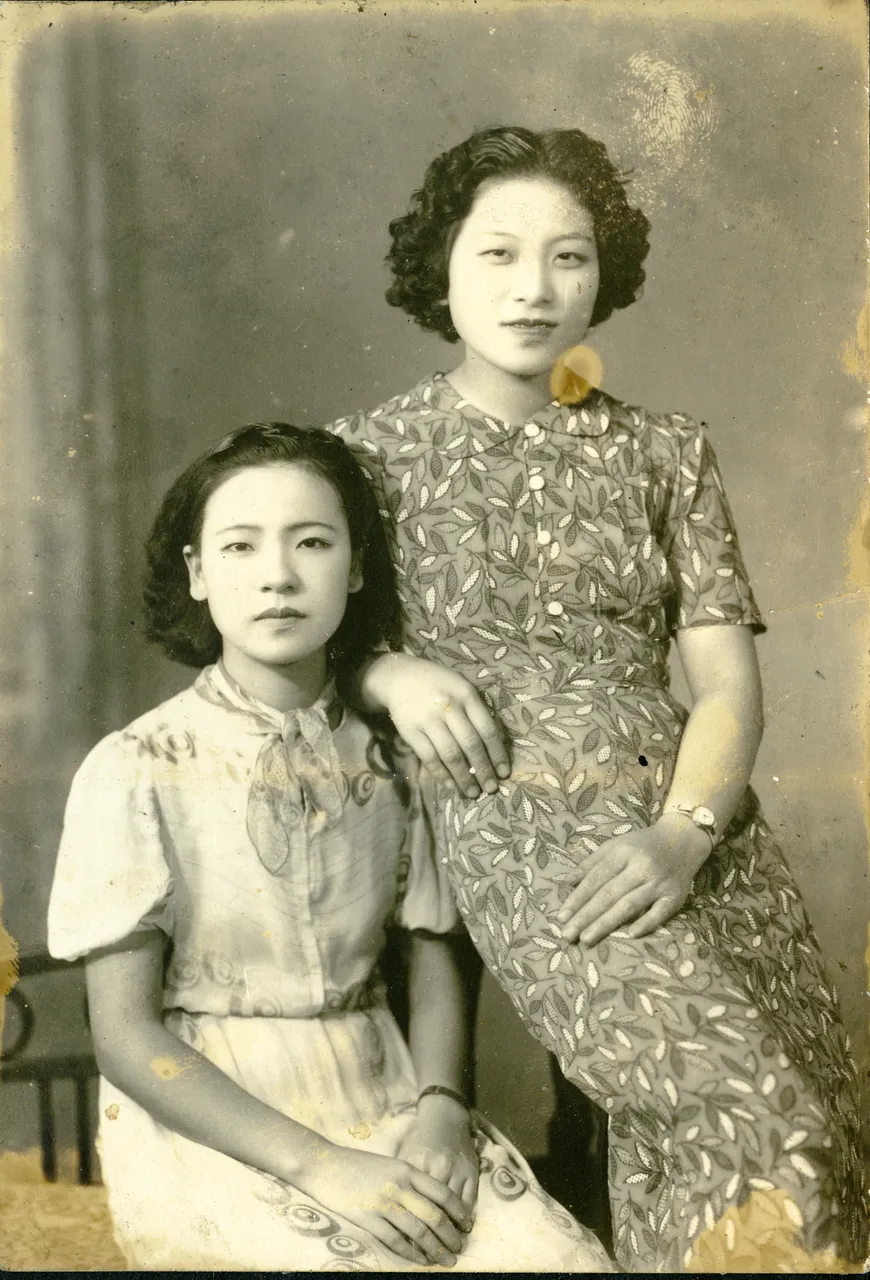 An old black-and-white portrait of two young women in patterned dresses, with a yellow blot, a fingerprint and spots
