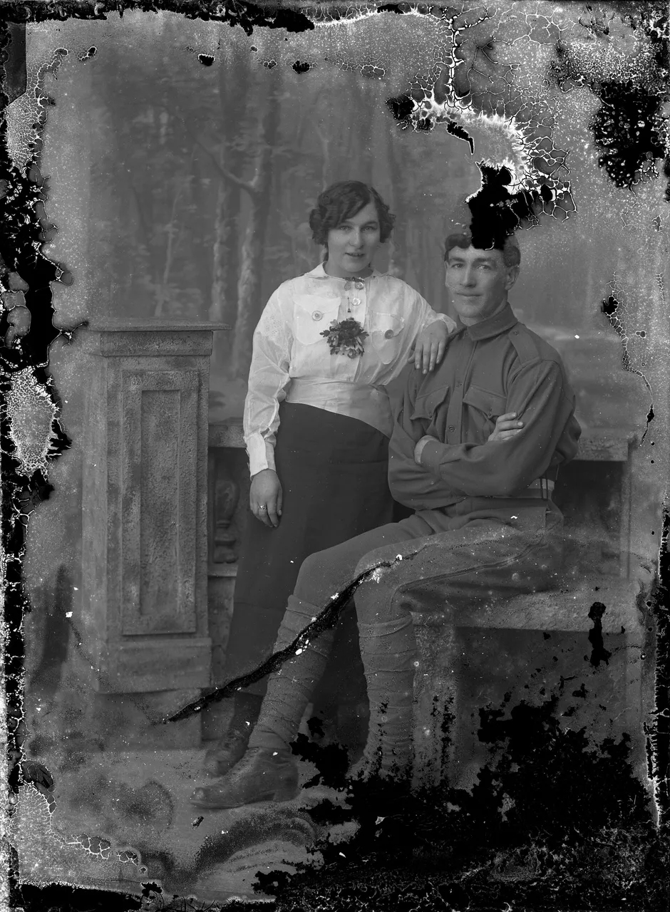 An old portrait of a soldier and a smiling woman, with flaking emulsion and a crack