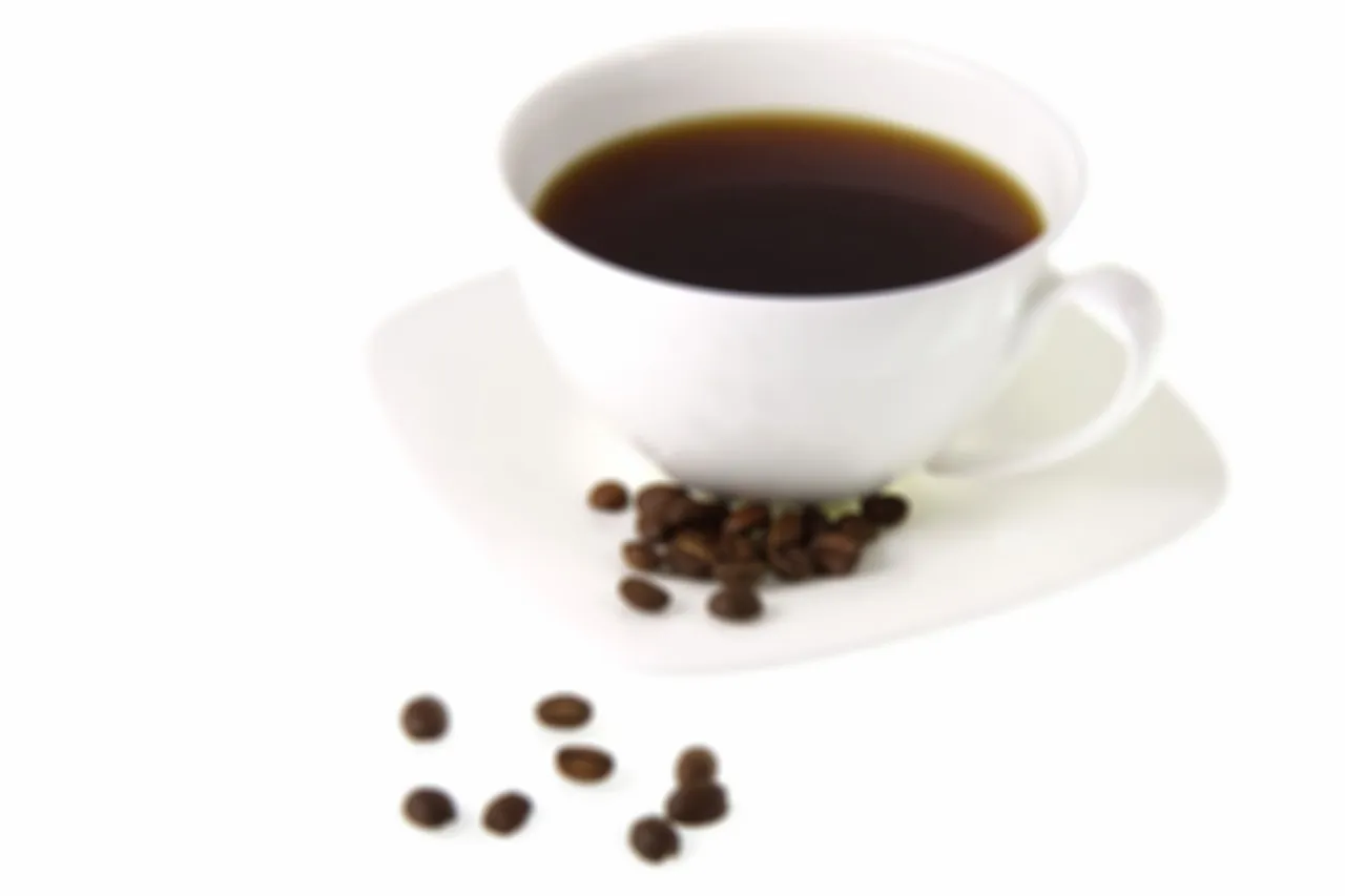 Una tazza di caffè nero sfocata con chicchi di caffè su sfondo bianco