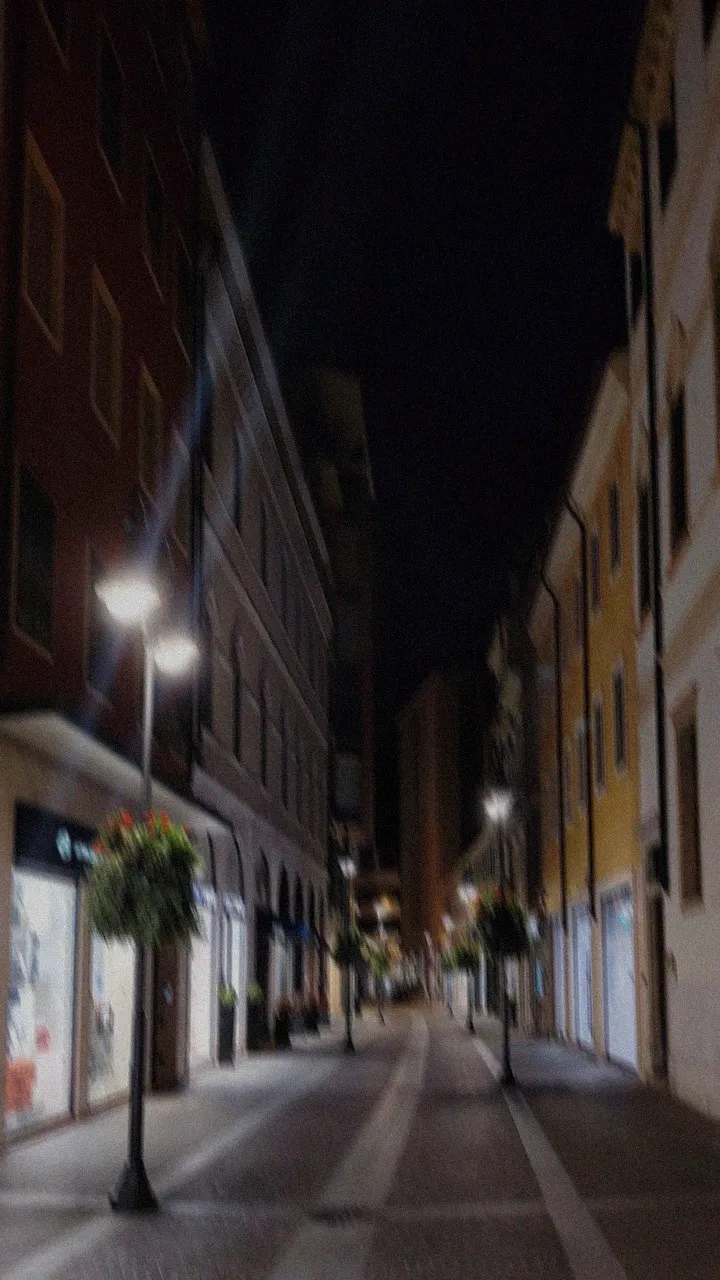 Una strada buia e mossa di notte, con lampioni e vasi di fiori appesi
