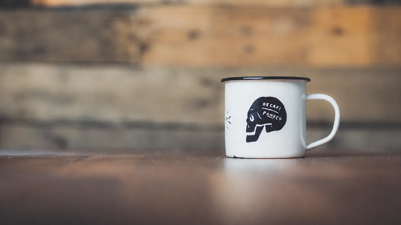 Tazza smaltata bianca su un tavolo di legno, con la stampa sulla tazza conservata